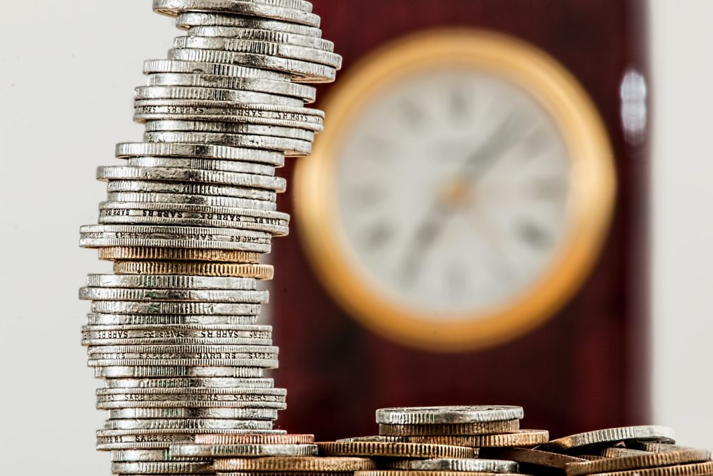 blurry clock in the background with a stack of coins in focus in the front