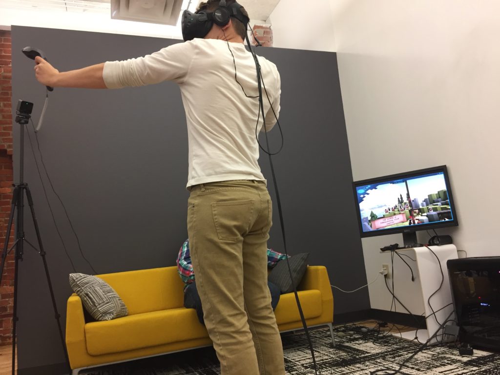 Man wearing virtual reality gear standing in front of a television screen