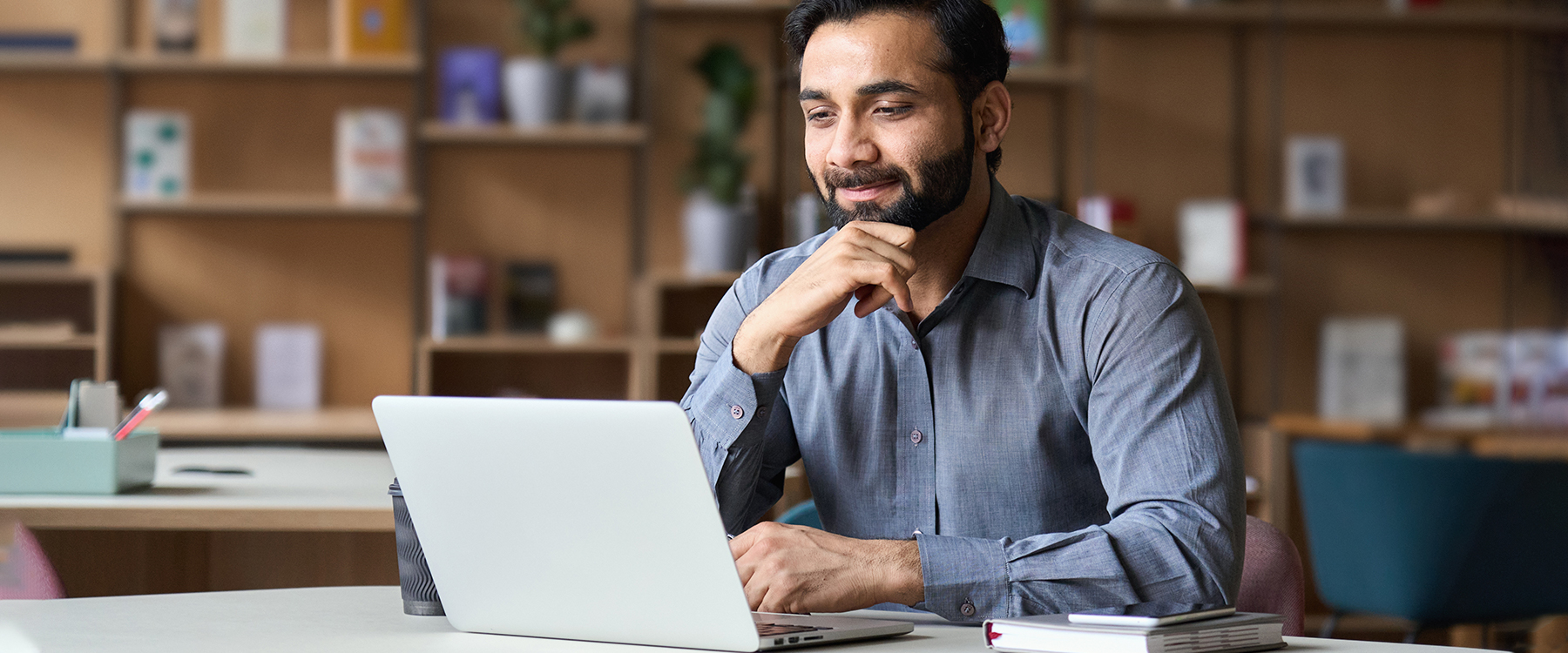 Man with beard and button up smiling at laptop in office