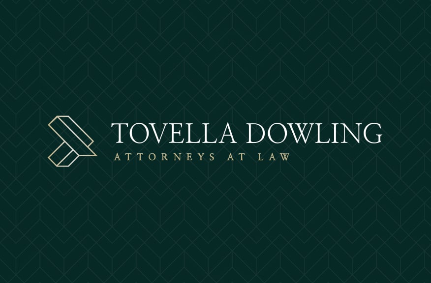 Logo for Tovella Dowling Attorneys at Law on a dark green patterned background, featuring a geometric gold emblem and elegant serif text in white and gold.