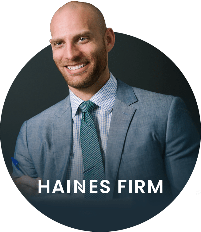 A smiling man in a suit and tie sits at a desk, holding a pen. The words HAINES FIRM are displayed across the lower part of the image.