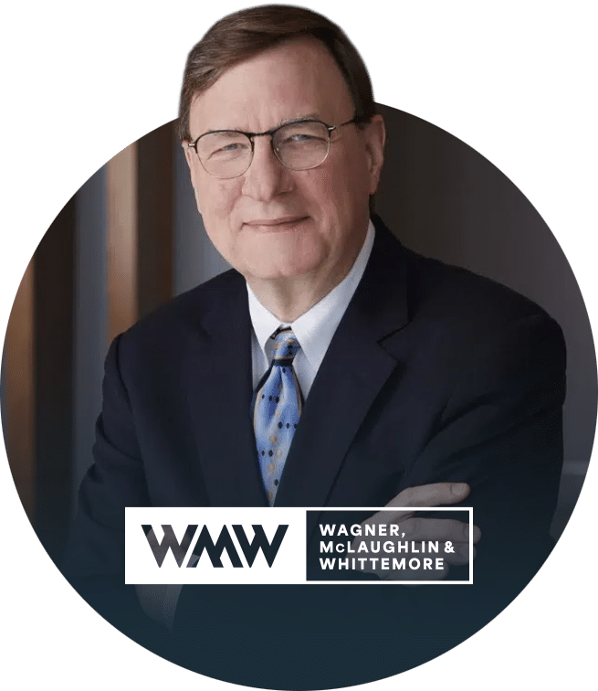 A middle-aged man wearing glasses, a dark suit, and a blue tie stands with arms crossed. The Wagner, McLaughlin & Whittemore logo appears at the bottom right of the image.